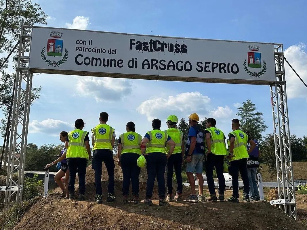Un gruppo di volontari con giubbotti fluorescenti posa sotto uno striscione dell'evento all'aperto in una giornata di sole La Varesina Emergenza Varese