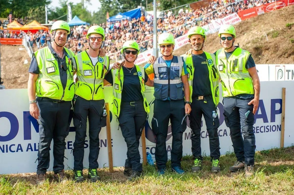 Sette membri dello staff dell'evento, con indosso giubbotti e caschi di sicurezza fluorescenti, posano insieme nell'area di arrivo di una gara all'aperto.