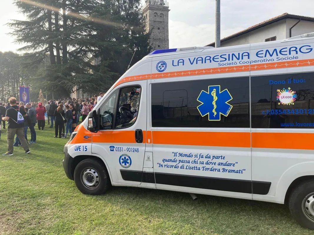 Un furgone ambulanza con simboli di emergenza parcheggiato sull'erba durante un raduno all'aperto La Varesina Emergenza Varese