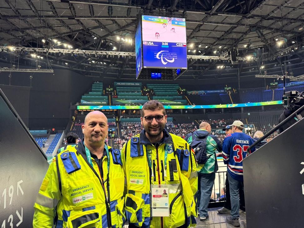 Quattro persone con giubbotti di sicurezza gialli in posa in una grande arena al coperto.