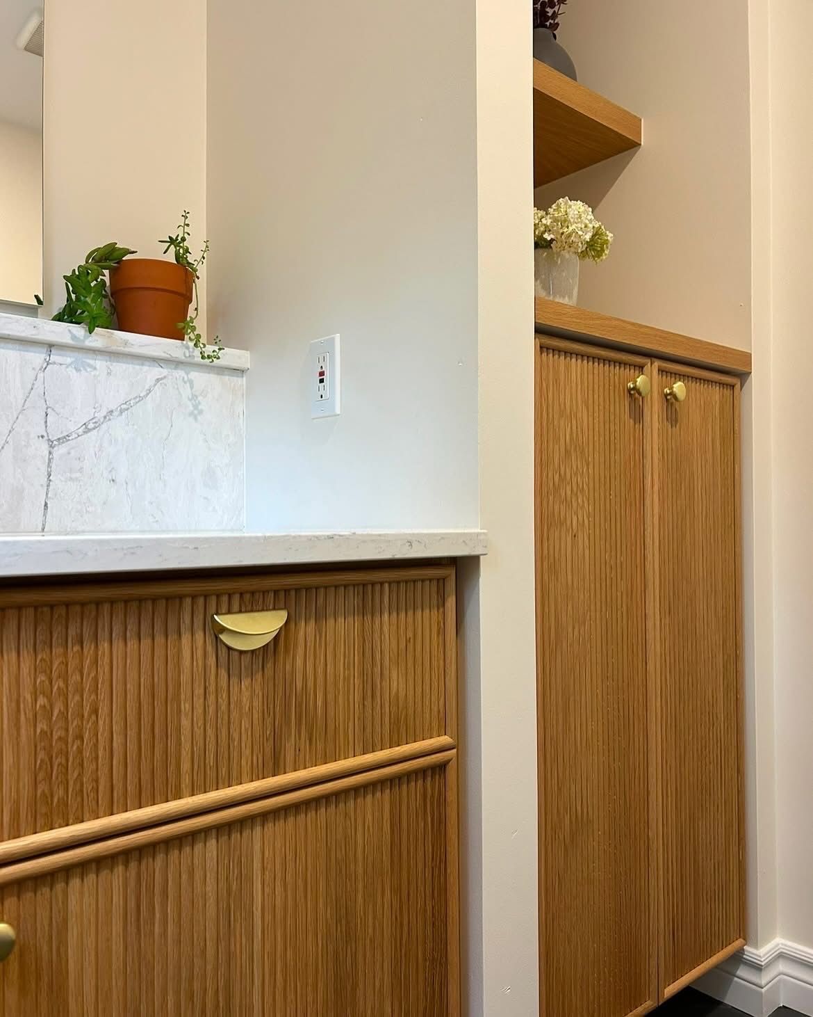 Armoires en bois avec un design texturé, des poignées en laiton et une étagère avec une plante et des fleurs.