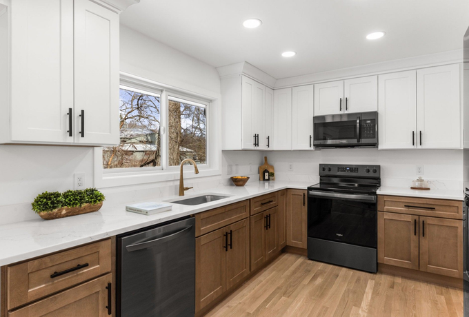 Modern white kitchen with black appliances, wood cabinets, and a window over the sink