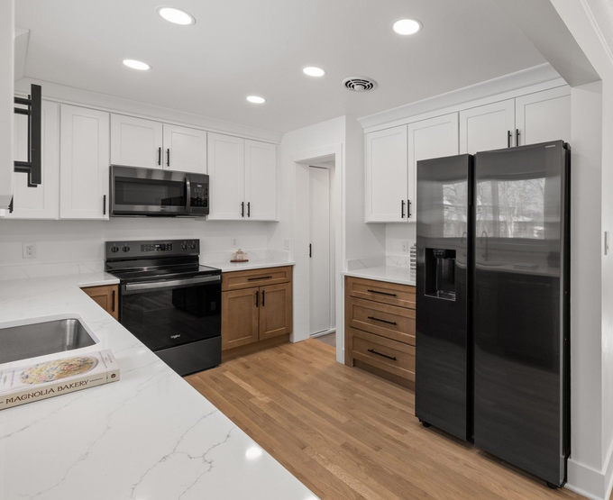 Remodeled kitchen featuring white upper cabinetry, natural wood lower cabinets, stainless steel appliances, and a side-by-side refrigerator.