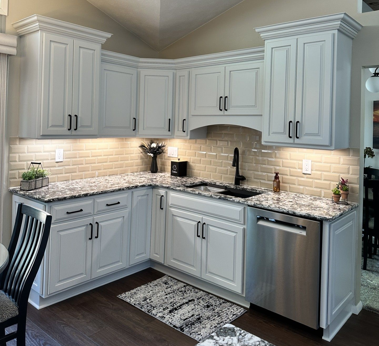 White kitchen cabinets with black hardware and granite countertops. Stainless steel appliances.