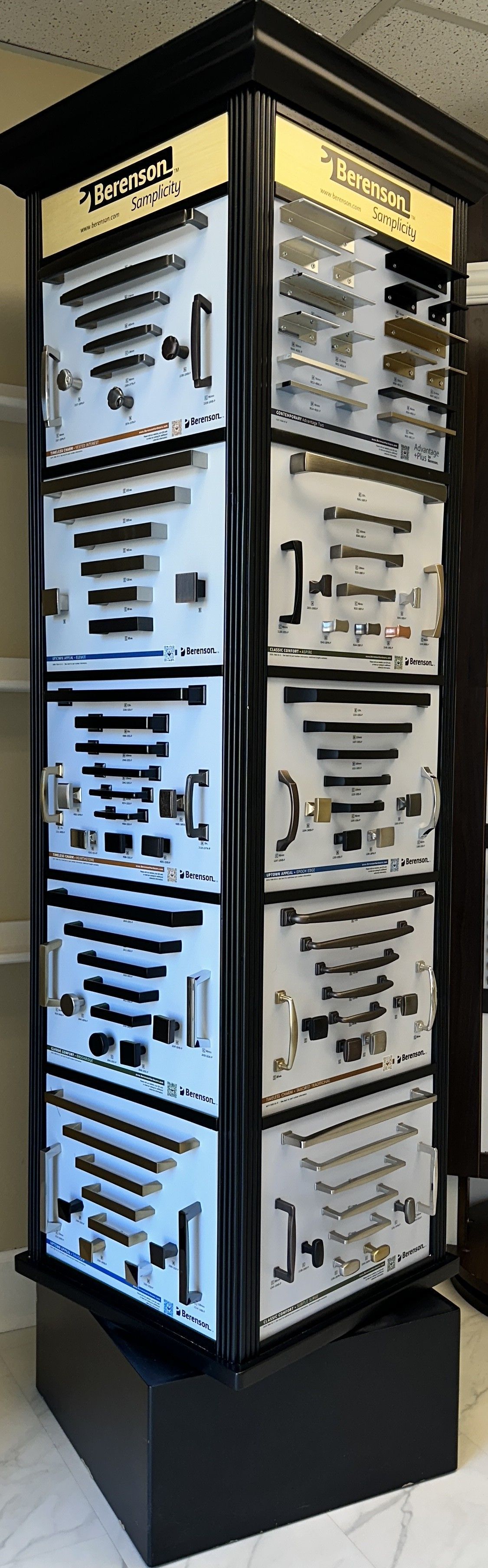 A tall, rotating display case showcasing hardware, likely in a retail setting. Black frame, light panels, and gold signage.