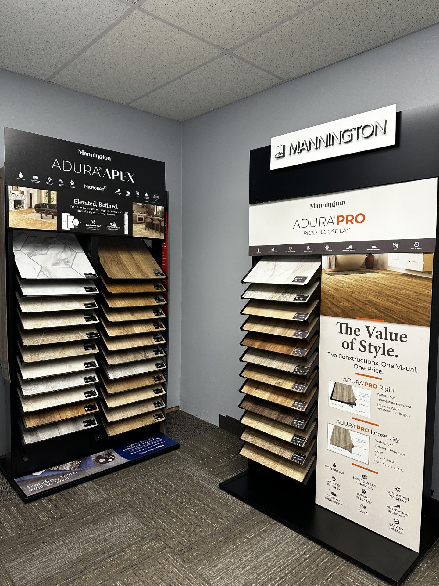 Display of ADURA luxury vinyl plank flooring samples in a showroom, various wood grain colors.