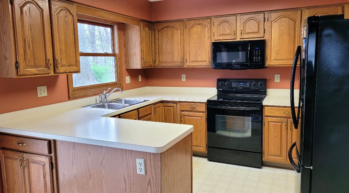 Kitchen with wooden cabinets, white countertops, black appliances, and a window.