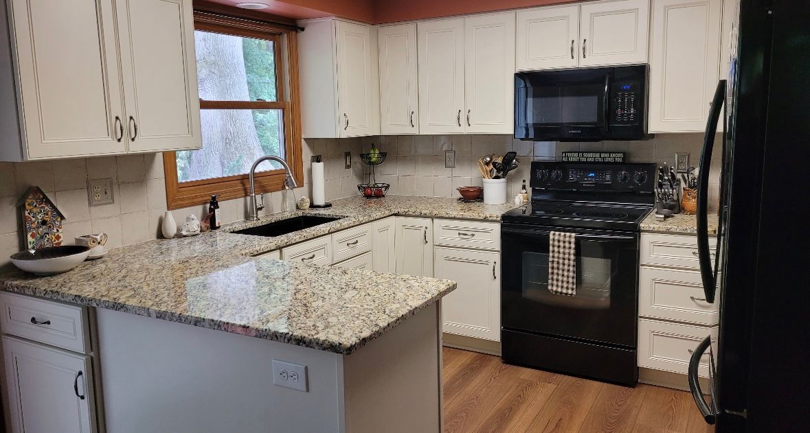 White kitchen with granite countertops, black appliances, and wooden flooring.