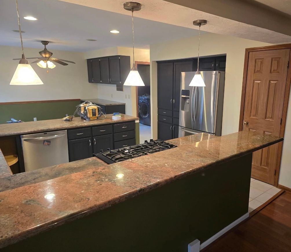 Kitchen with dark cabinets, granite countertops, stove, refrigerator, pendant lights, and brown door.