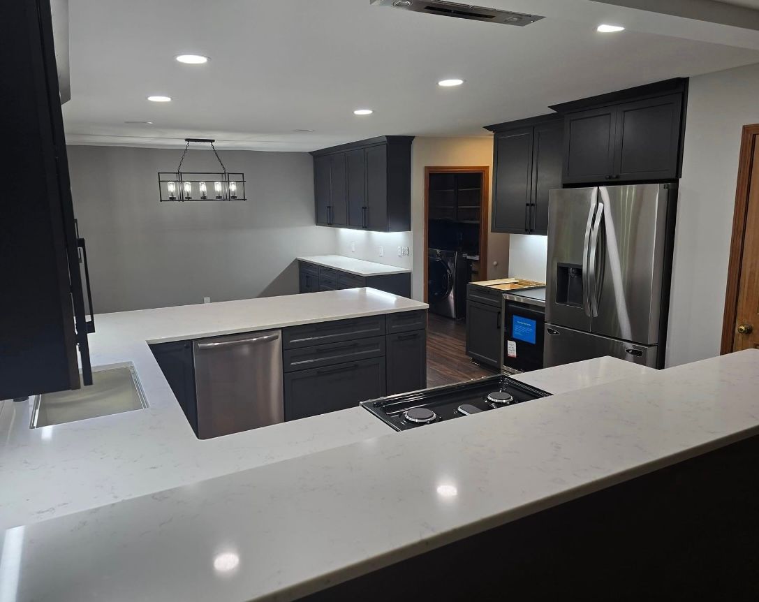 Modern kitchen with dark gray cabinets, white countertops, and stainless steel appliances.
