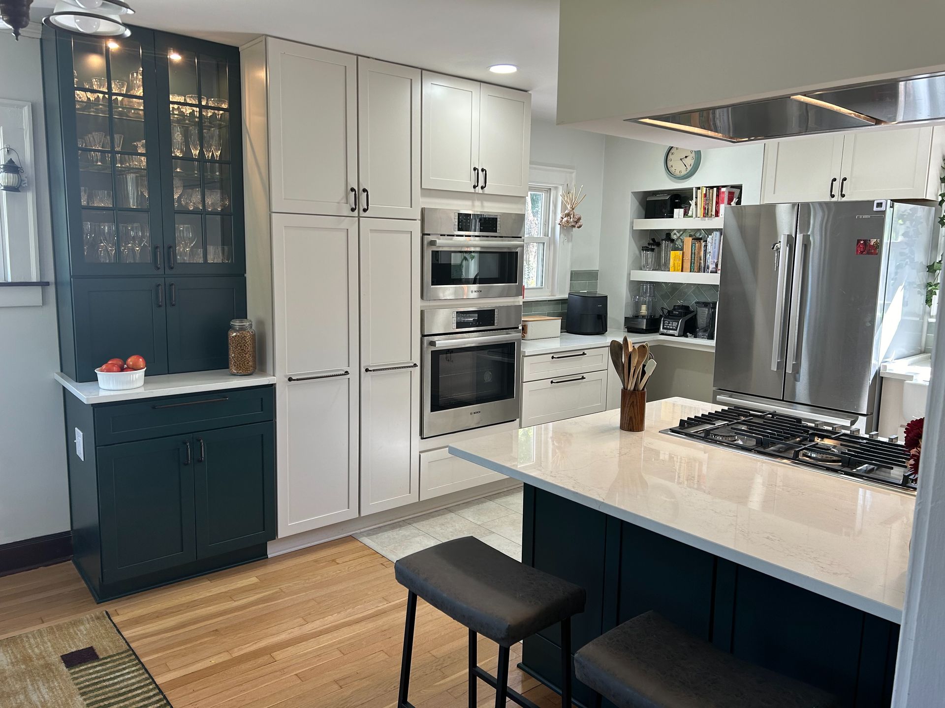 Modern kitchen with white and dark green cabinets, stainless steel appliances, and a central island with stools.
