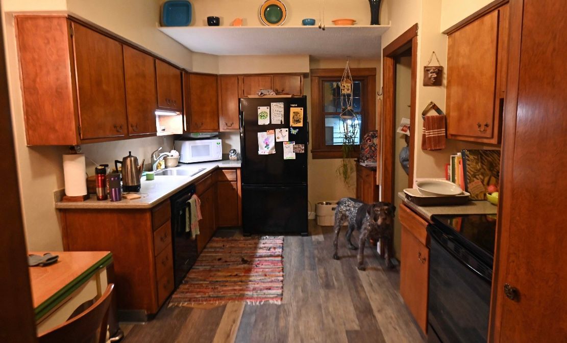 Kitchen with brown cabinets, black appliances, and a dog standing in the doorway.