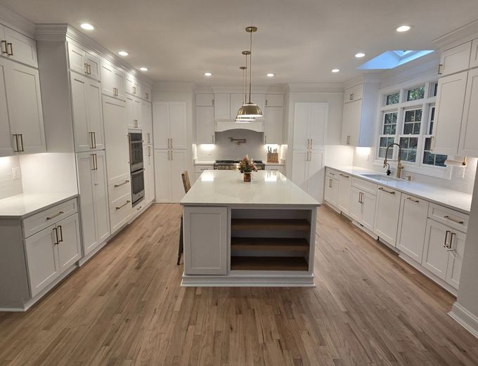 Bright white kitchen with a large island, white cabinets, light wood floor, and a skylight.