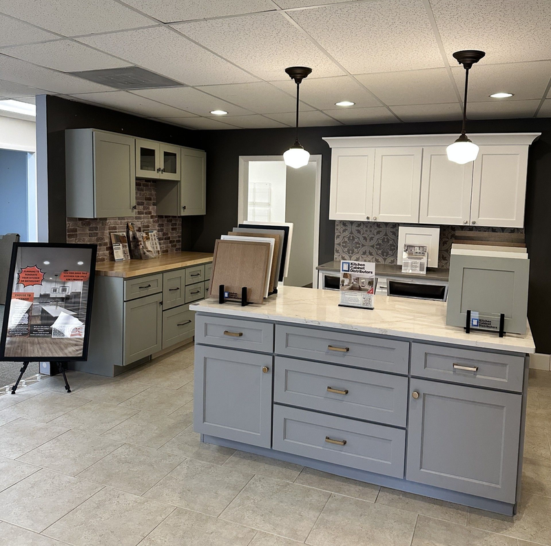 Kitchen showroom with cabinets in light blue, white, and gray. Countertops, samples, and lighting.