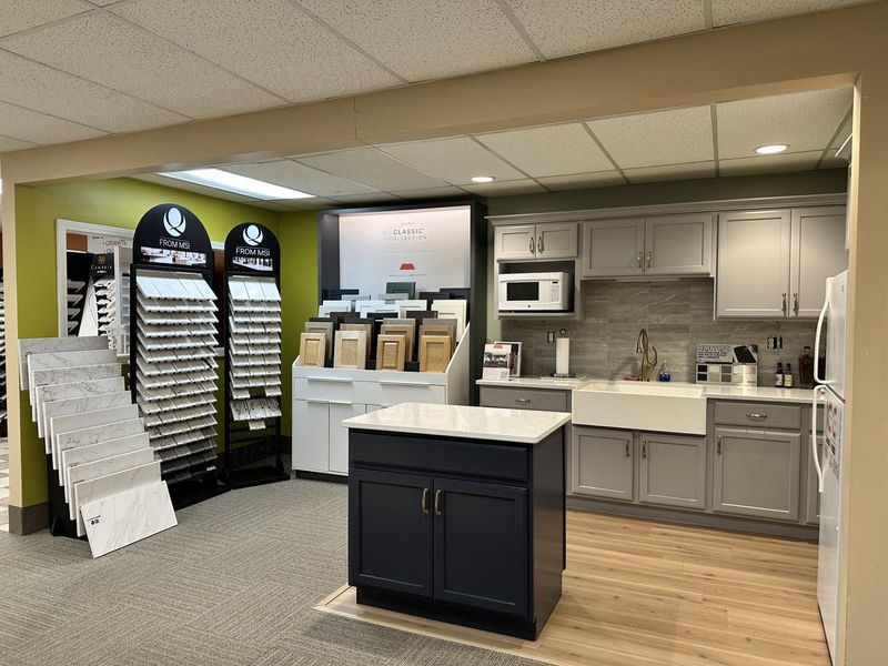 Kitchen showroom with displays of cabinets, countertops, and a small kitchen model with appliances.