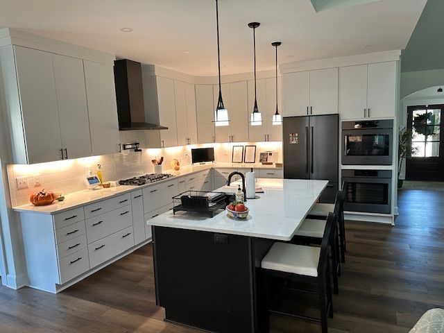 Modern kitchen with white cabinets, dark island, and stainless steel appliances.