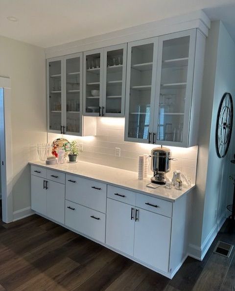 White kitchen cabinets with glass doors, countertop, and backsplash, illuminated by lights.