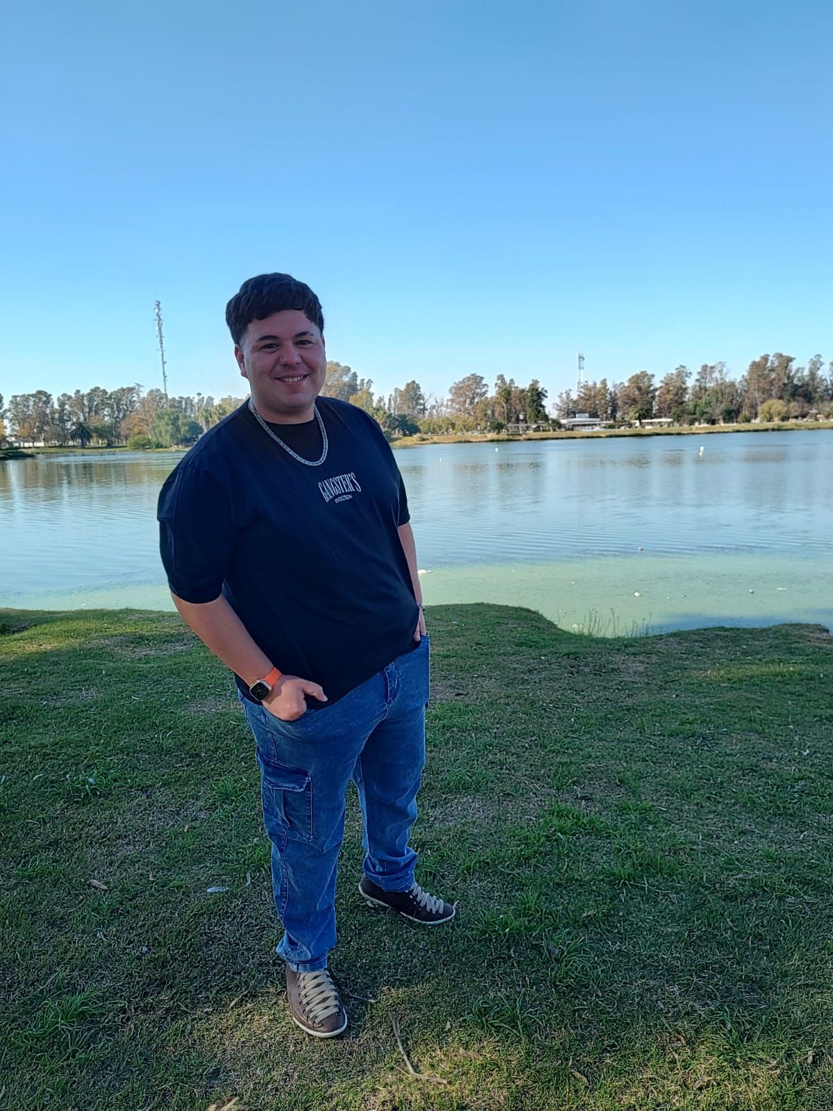 Hombre de pie sobre el césped junto al lago, sonriendo.