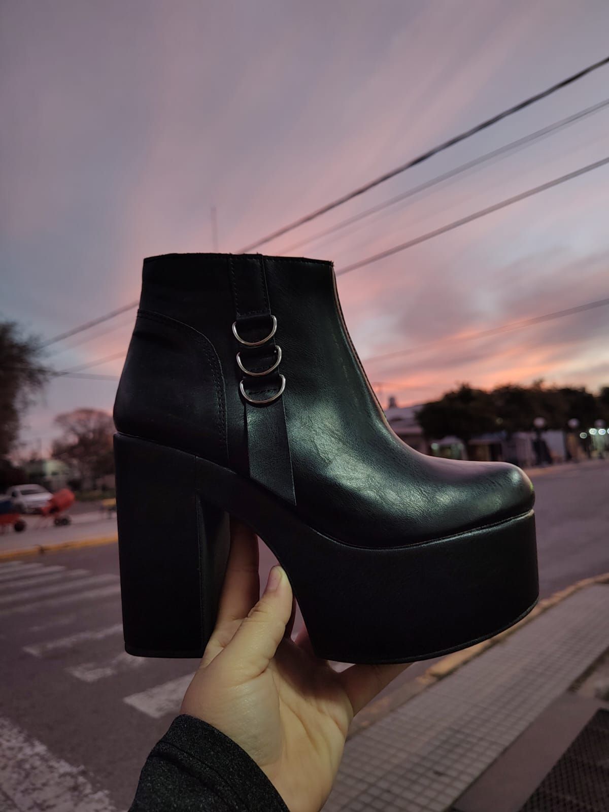 Bota de plataforma negra sostenida en la mano contra el cielo del atardecer.
