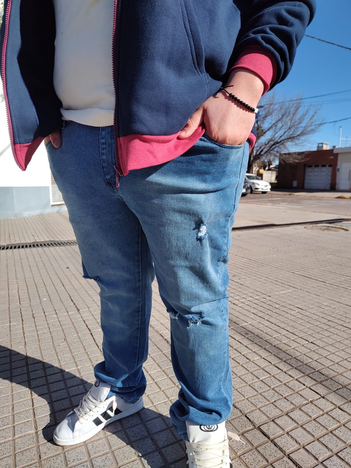 Persona con jeans azules, una chaqueta azul marino con detalles rojos y zapatillas blancas.