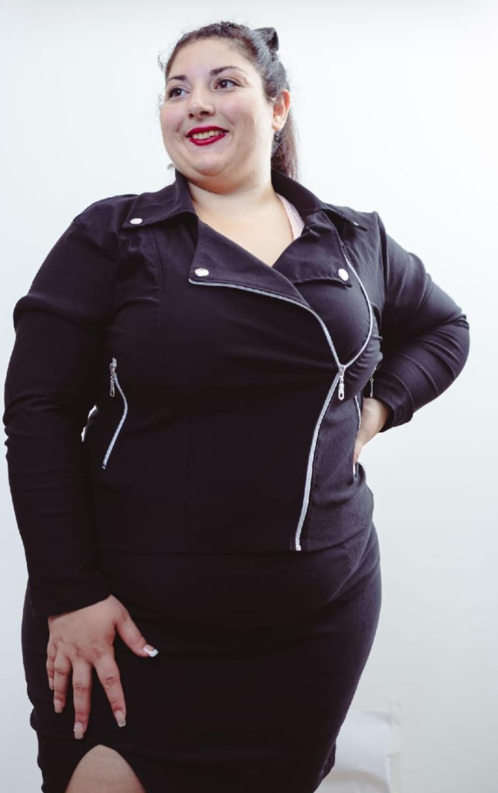 Mujer con chaqueta y falda negras, sonriendo y posando sobre un fondo blanco.