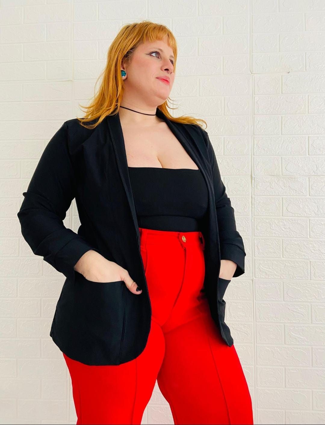 Mujer con blazer negro, top negro y pantalones rojos, con las manos en los bolsillos.
