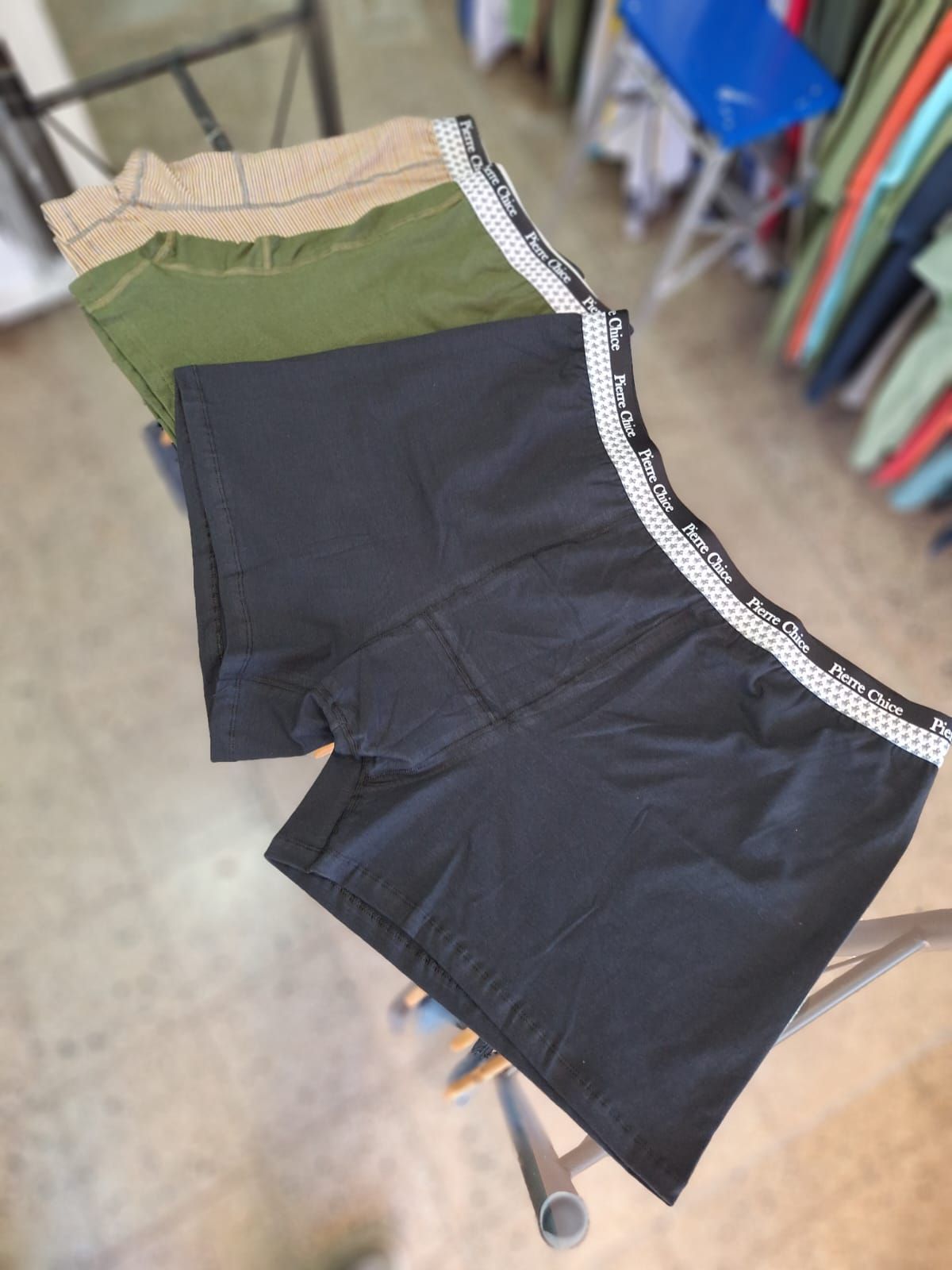 Tres pares de calzoncillos bóxer para hombre, de color negro, verde y tostado, apilados en un soporte de metal en una tienda.