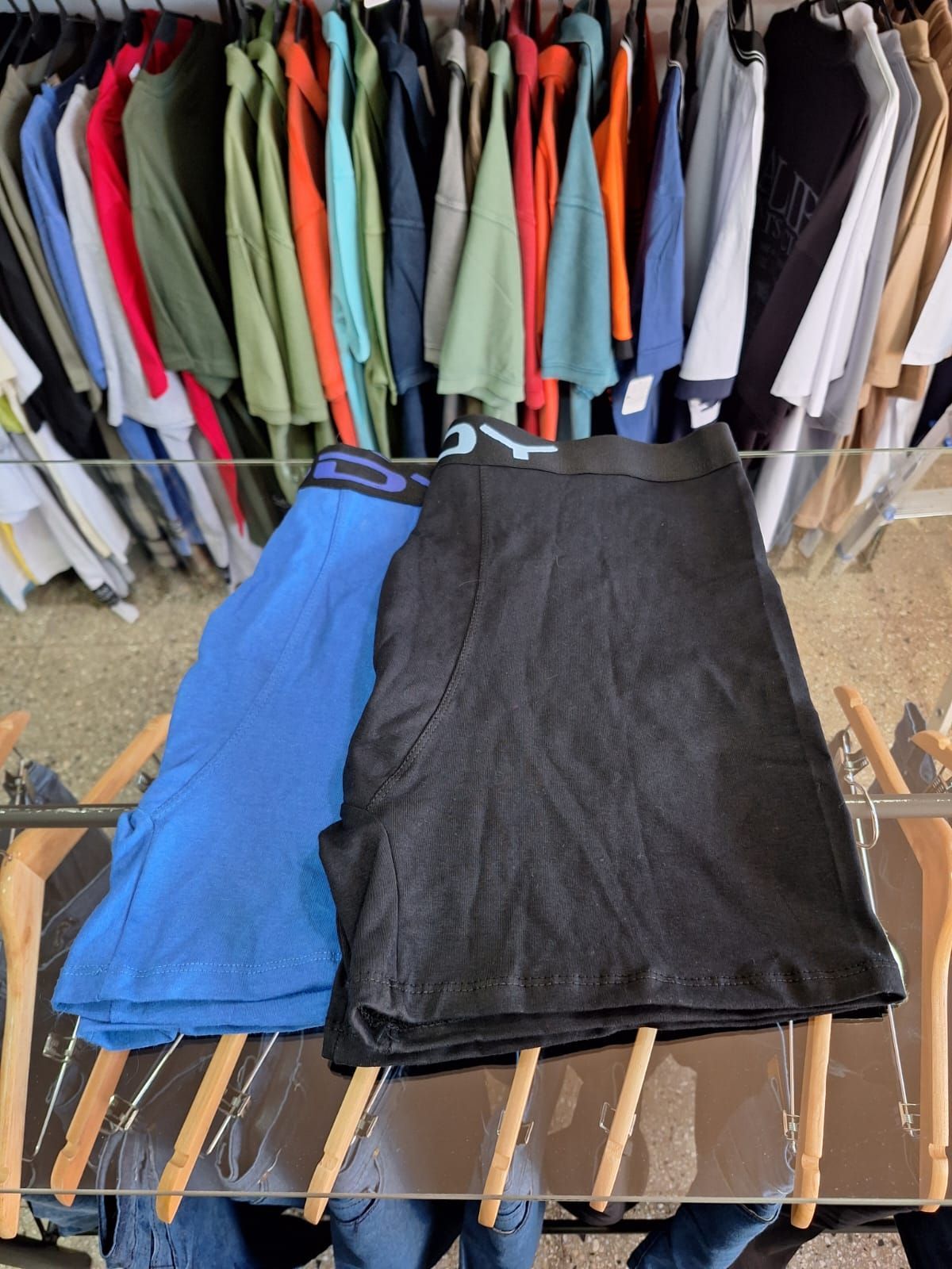 Dos pares de calzoncillos bóxer, uno azul y otro negro, en un expositor con percheros al fondo.