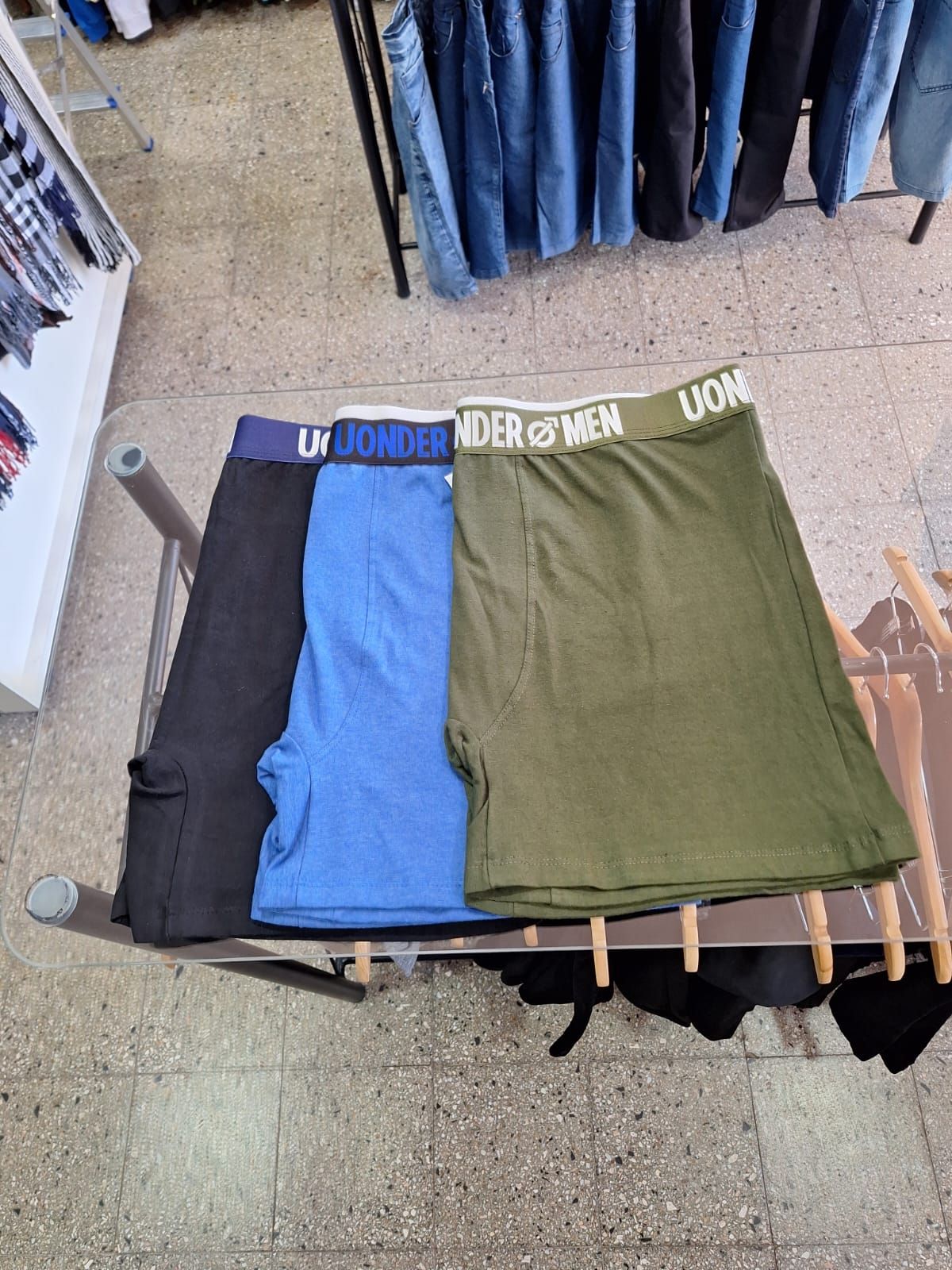 Tres pares de calzoncillos bóxer: negro, azul y verde, expuestos en un perchero de ropa en una tienda.