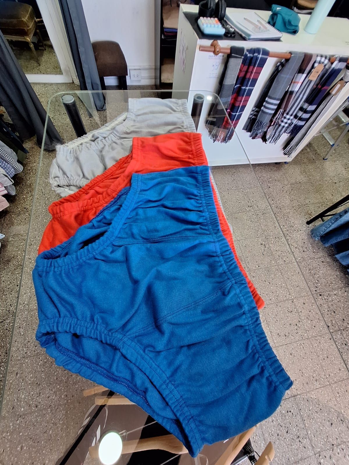 Tres pares de calzoncillos coloridos: azul, rojo y gris, dispuestos sobre una mesa de cristal en una tienda.