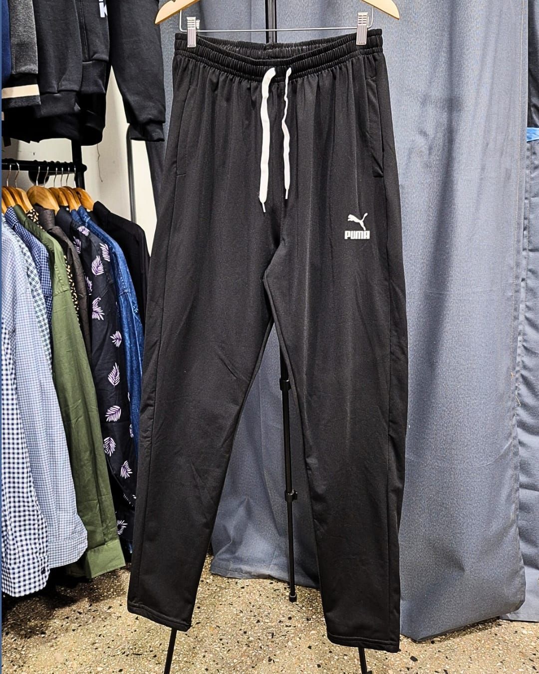 Pantalones deportivos Puma negros colgados en un perchero, con cordón blanco y logotipo.