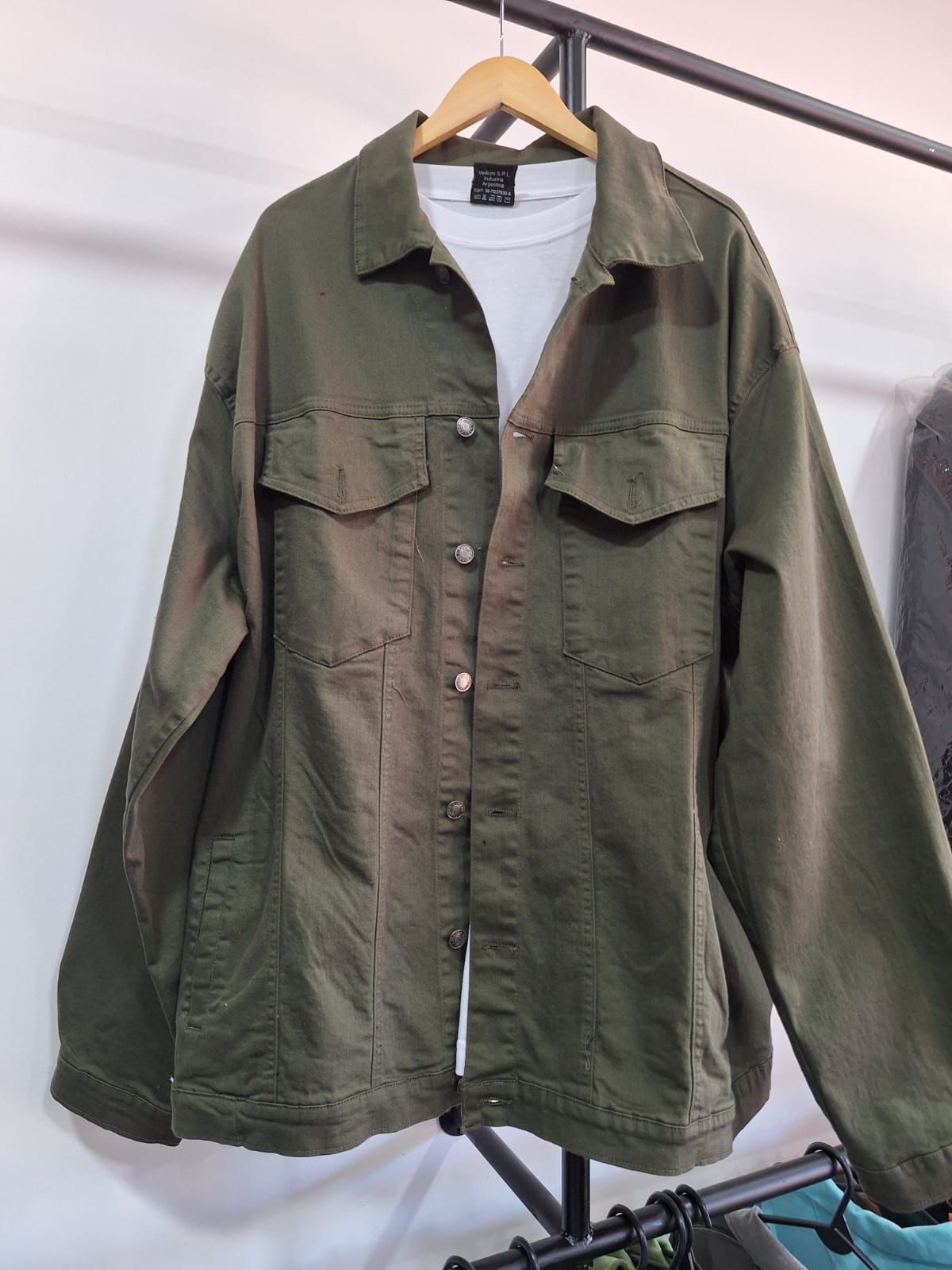 Chaqueta oversize de color verde oliva sobre una camisa blanca, colgada en una percha de madera.