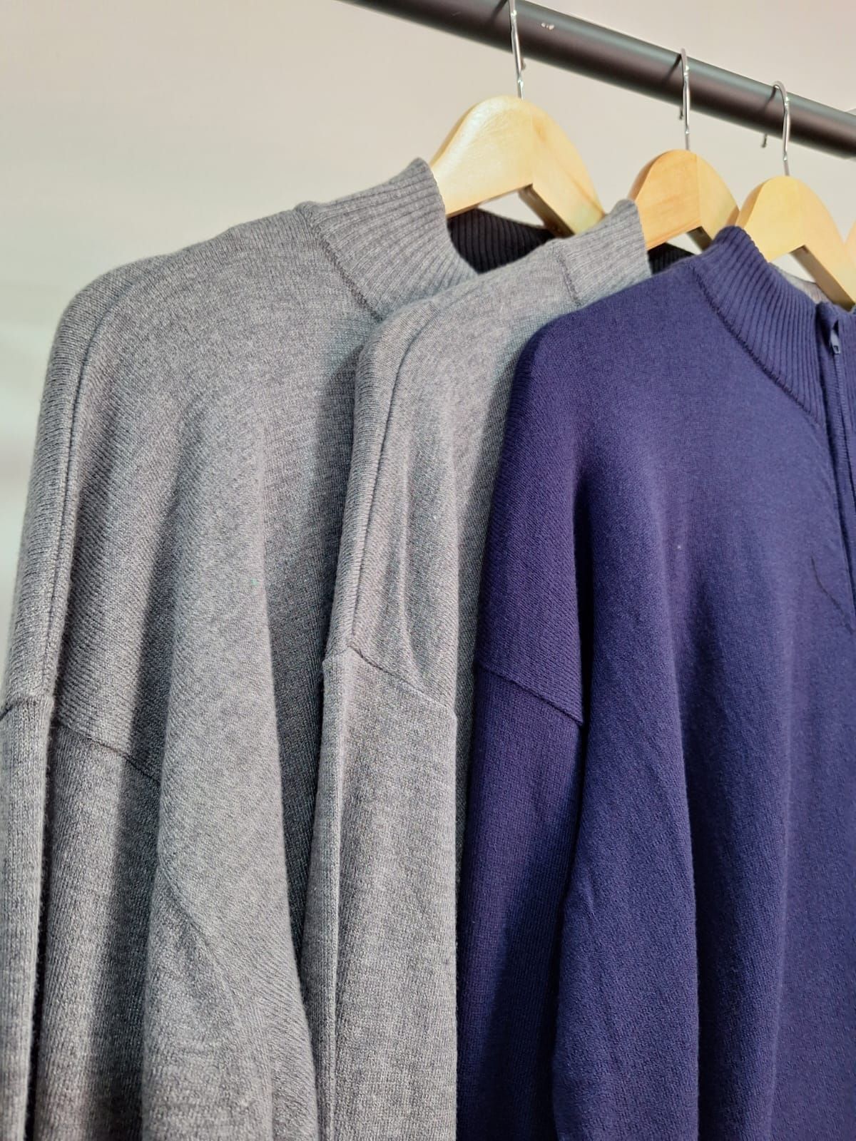 Tres suéteres, gris y azul marino, cuelgan de un perchero de madera.
