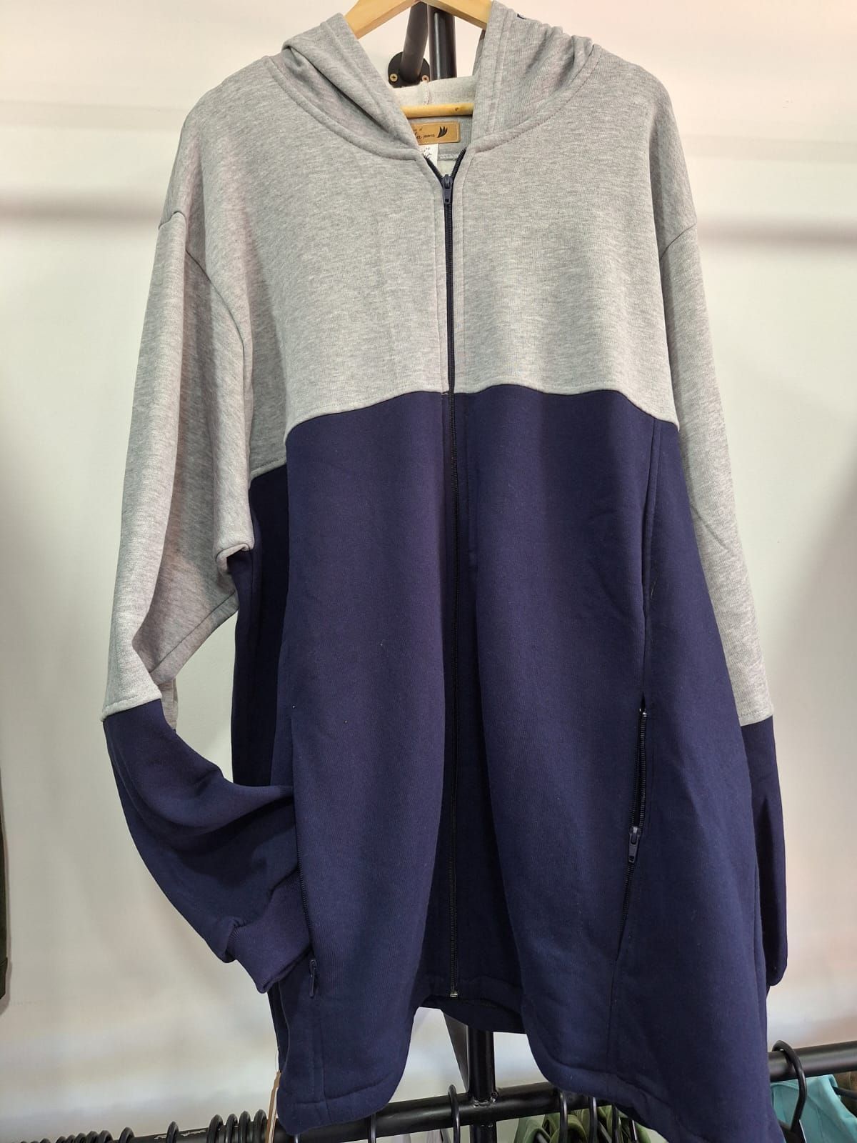 Sudadera con capucha y cremallera de color gris y azul marino colgada en un perchero.