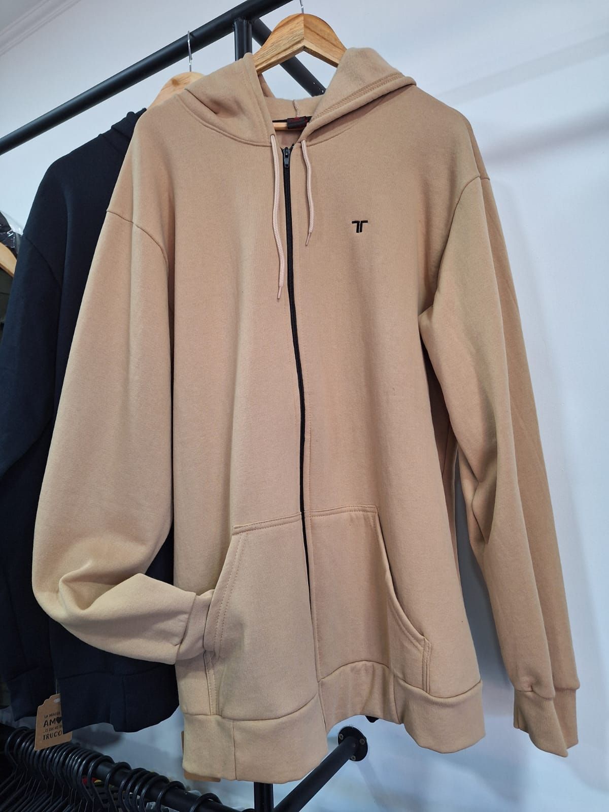 Sudadera con capucha color canela y cremallera colgada en un perchero.