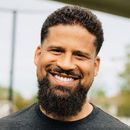 Smiling man with curly hair and beard outdoors on a blurred street background