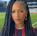 Portrait of a woman with long braids in a red-and-black jersey at a soccer stadium