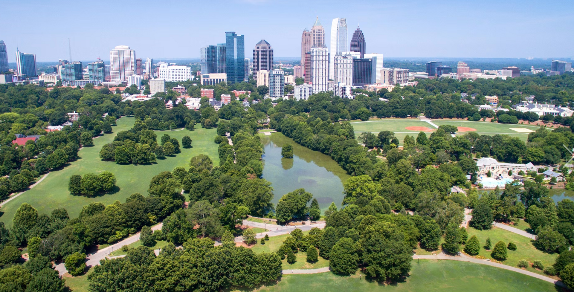 Aerial view of a city park with a pond, trees, and downtown skyline in the background