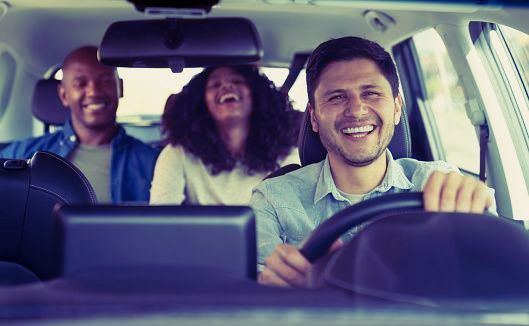 Man driving, happy couple in the backseat sharing a laugh.