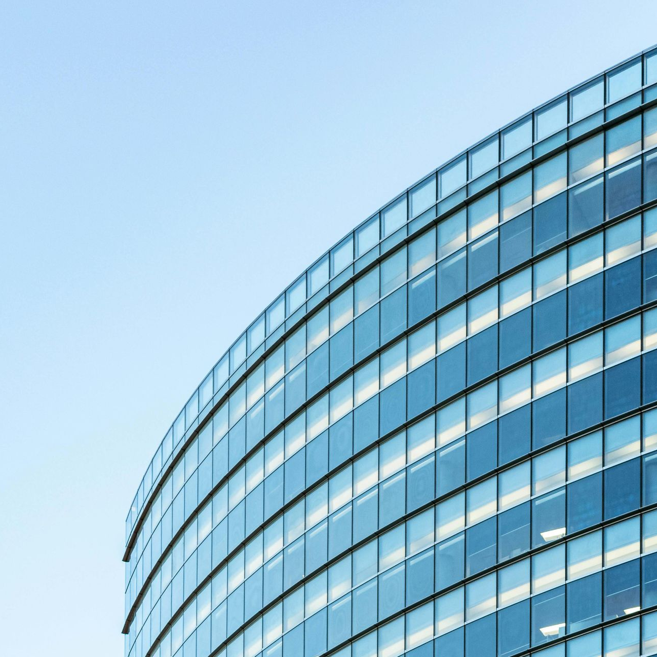 A curved, modern glass office building exterior reflecting the blue sky against a clear background.