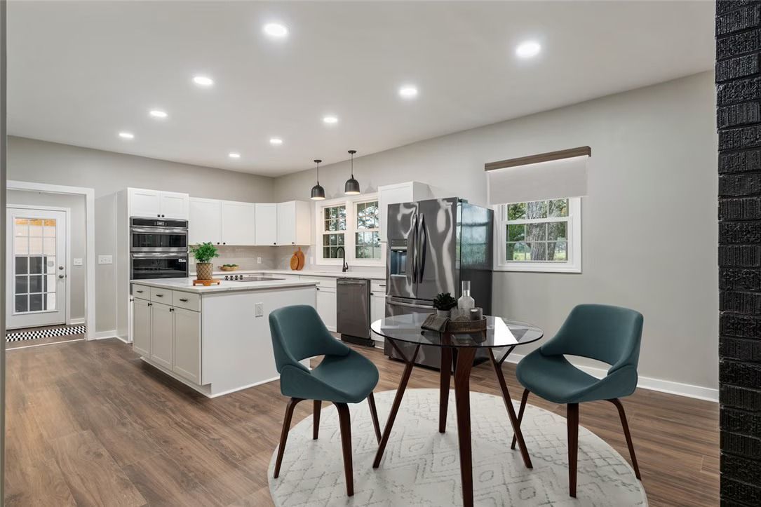 Open kitchen and dining area with white cabinets, wood floors, and a small round table with teal chairs.