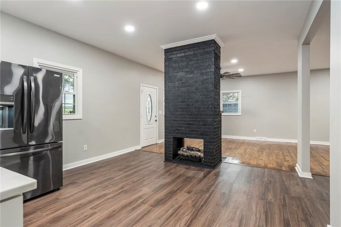 Modern open-plan living room with dark wood floors, black brick fireplace, and stainless steel refrigerator