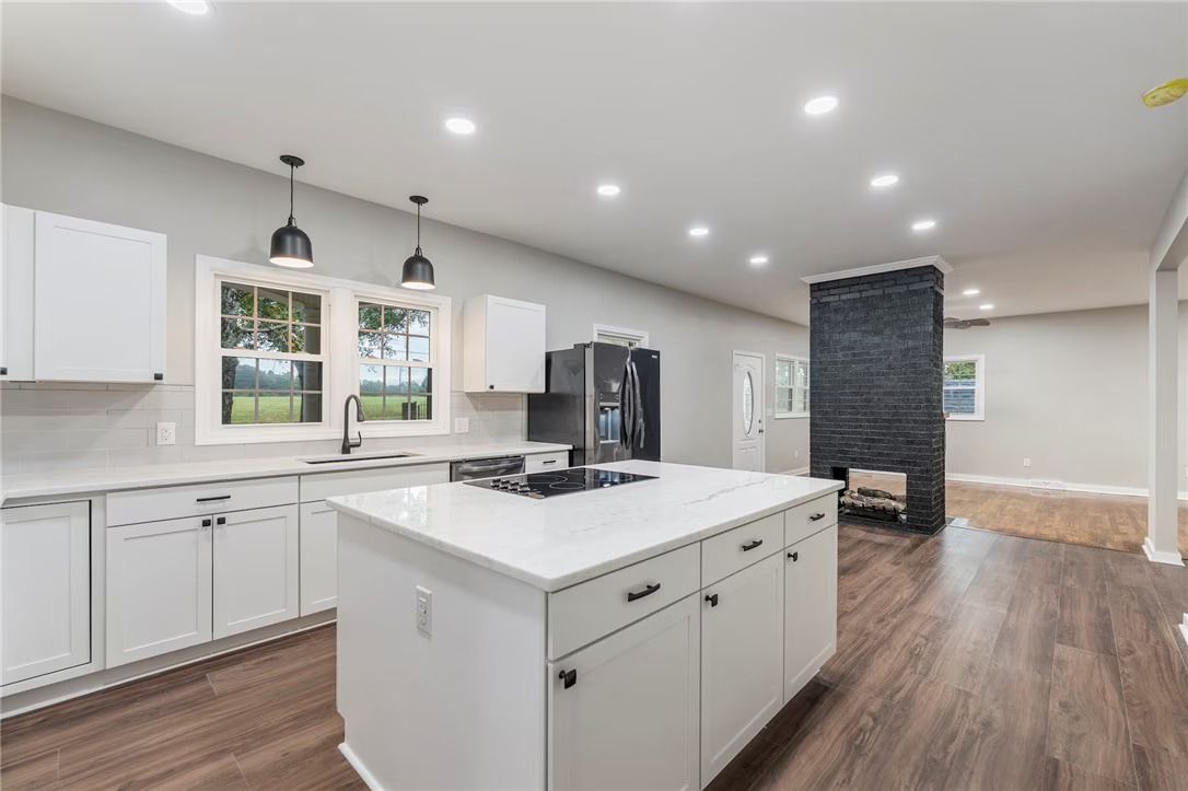 Bright modern kitchen with white cabinets, large island, dark fireplace, and wood floors