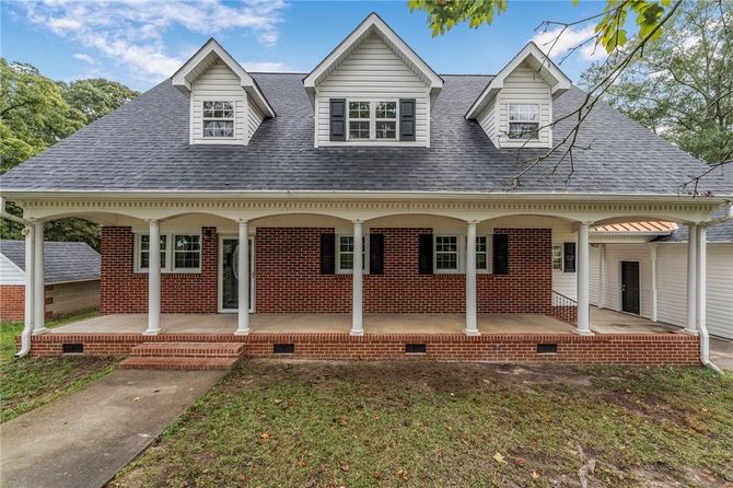 Gray two-story house with a large covered front porch, white trim, and brick base, seen from the front.