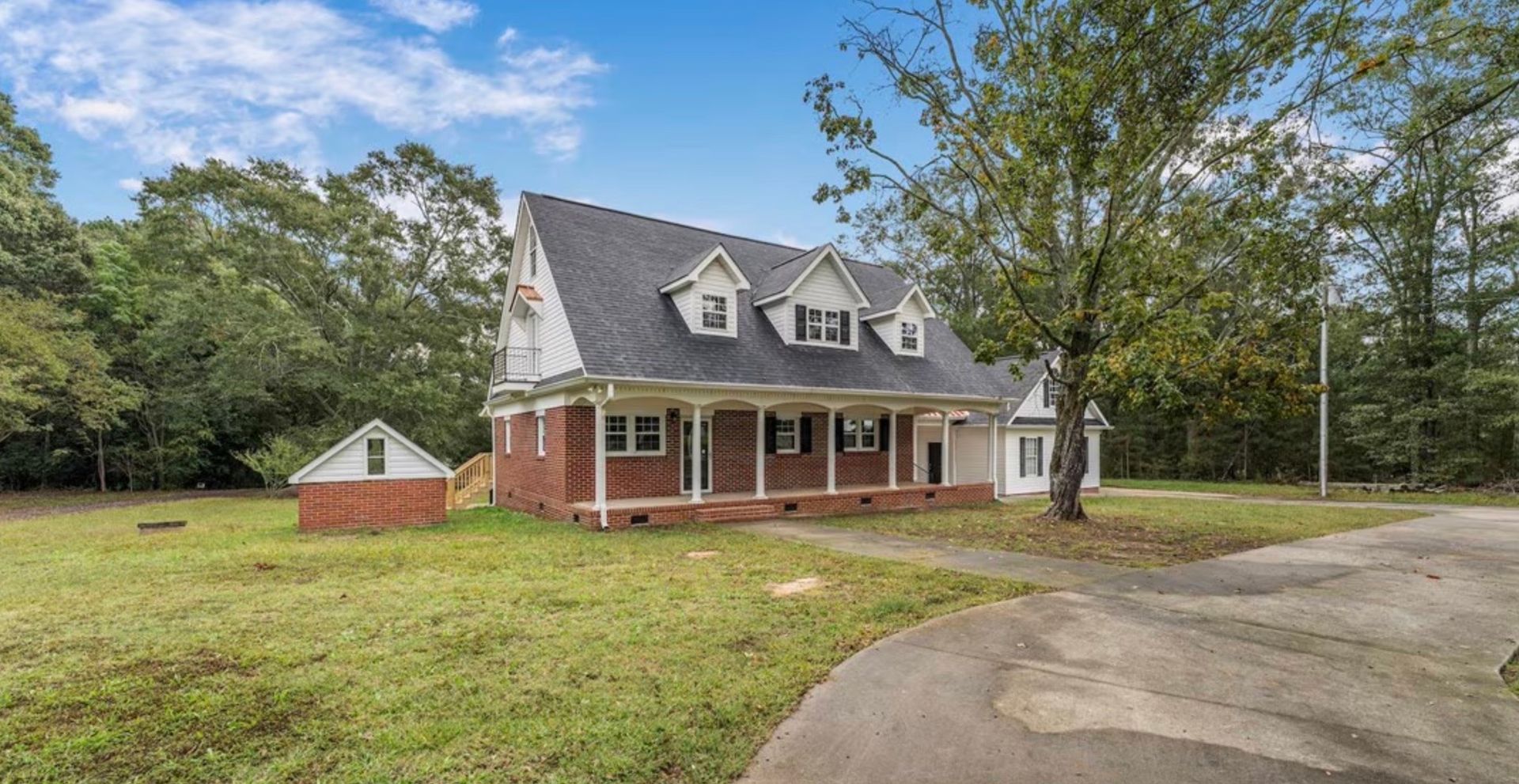 Two-story brick house with gray roof, front porch, and large lawn by a curved driveway