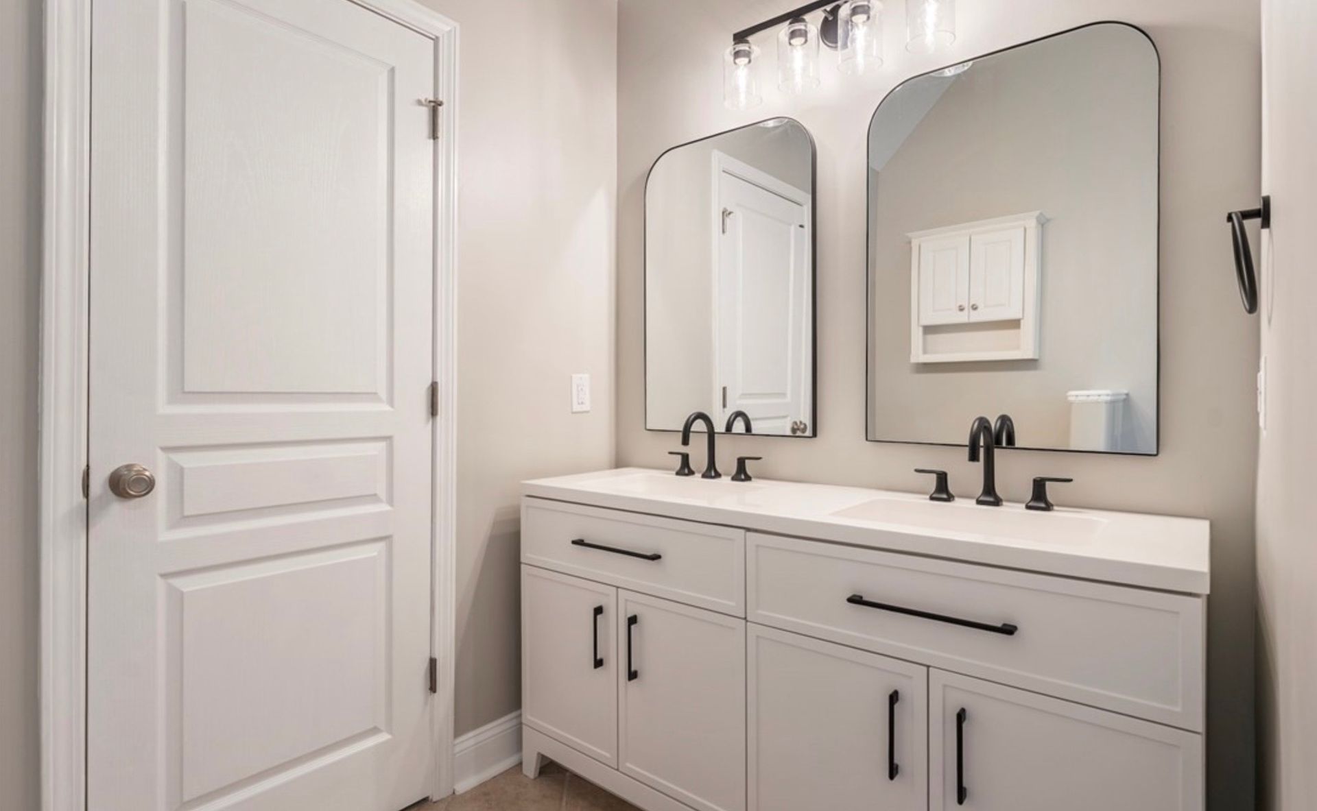 Modern bathroom vanity with double sinks, large mirrors, and white cabinetry in a bright beige room