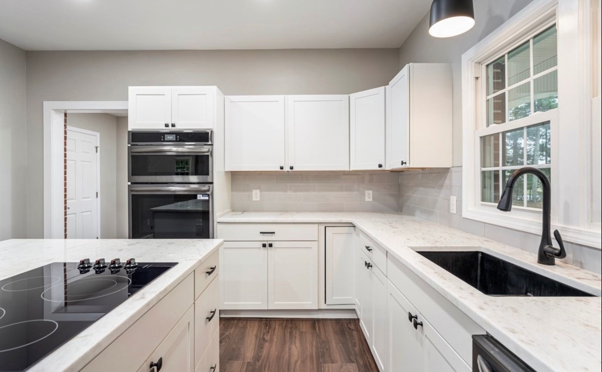 Bright modern white kitchen with black countertops, stainless appliances, and a window over the sink
