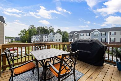 Balcony deck with patio table, chairs, and covered grill overlooking neighboring townhouses under a blue sky