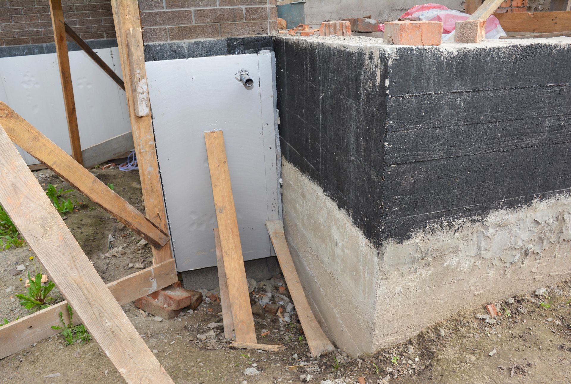 Partially built concrete foundation corner with black waterproofing and wooden supports