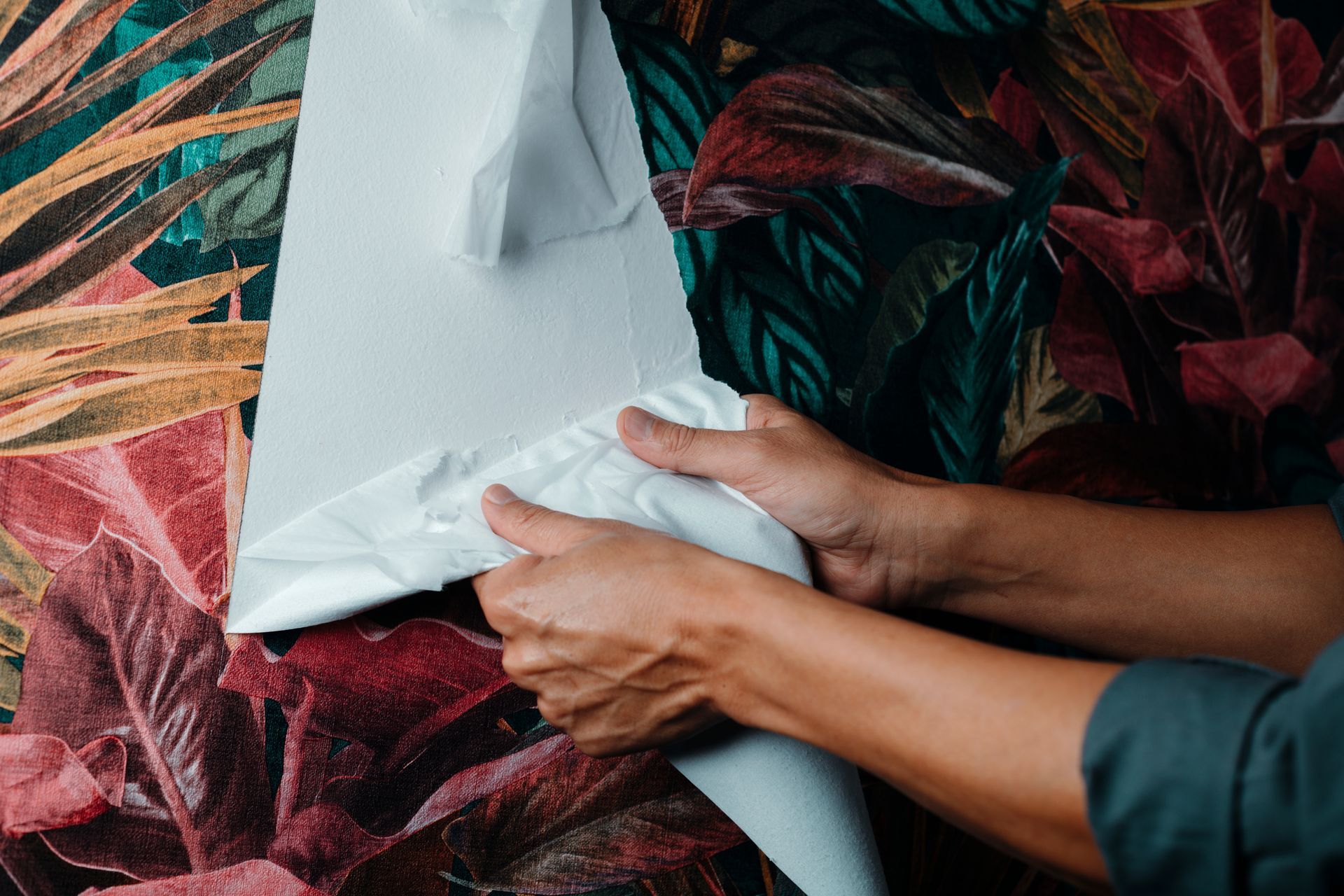Hands stretch white fabric over a colorful leafy backdrop.